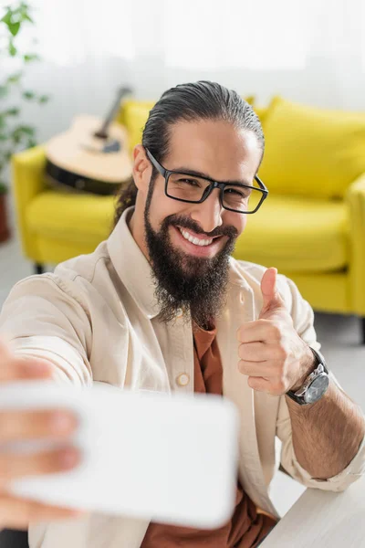 Happy latin man showing thumb up while taking selfie on blurred smartphone — Stock Photo