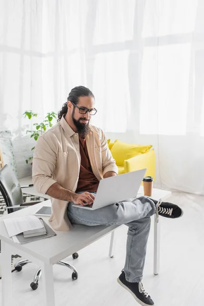 Freelance ispanico in occhiali da vista digitando sul computer portatile mentre seduto sulla scrivania di lavoro a casa — Foto stock