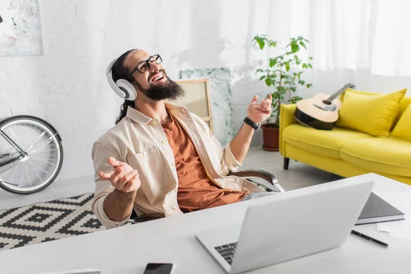 Complacido latino freelancer en auriculares escuchando música cerca de laptop en casa - foto de stock