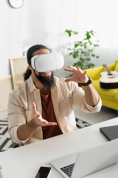 Latin freelancer gesturing in vr headset near blurred laptop in home — Foto stock