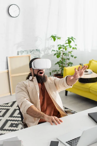 Asombrado hombre hispano haciendo gestos mientras juega en vr auriculares en la sala de estar - foto de stock