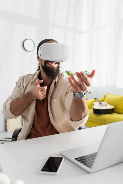 Allegro ispanico freelancer tiro da fucile virtuale durante il gioco in auricolare vr vicino al computer offuscata — Foto stock