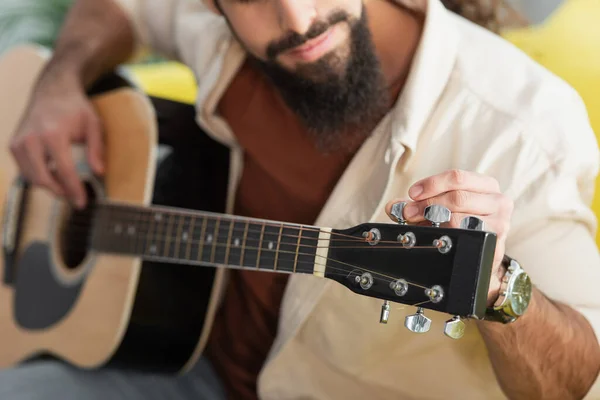 Ausgeschnittene Ansicht eines verschwommenen Musikers, der zu Hause Gitarre stimmt — Stockfoto