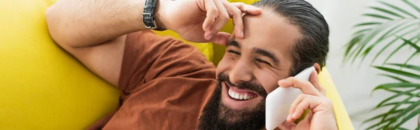 Barbudo latino riendo mientras habla en el teléfono móvil con los ojos cerrados, pancarta - foto de stock