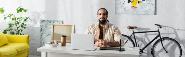 Freelancer latino barbudo sentado perto de laptop e tablet gráfico em estúdio em casa, banner — Fotografia de Stock