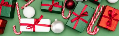 Renkli hediye kutularının panoramik konsepti, baston şekerler ve yeşil arka planda noel topları, üst manzara
