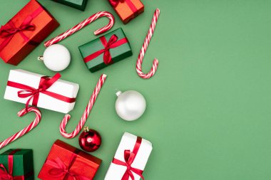 Çok renkli hediye kutularının, baston şekerlerin ve yeşil arka planda noel balolarının üst görüntüsü