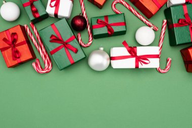 Renkli hediye kutularının, baston şekerlerin ve yeşil arka planda fotokopi alanının olduğu noel toplarının üst görüntüsü