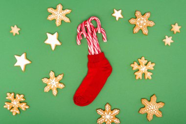top view of red christmas stocking with candy canes near backed stars and snowflakes on green background clipart