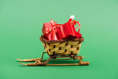 Kırmızı hediye kutuları ve hasır sepette Noel Baba şapkası yeşil arka planda dekoratif kızak