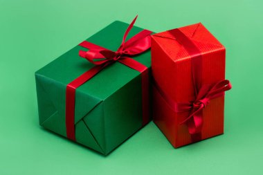 two colorful present boxes with red ribbons and bows on green background clipart