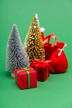 Gümüş ve altın dekoratif Noel ağaçları hediye kutularının yanında, çuval ve alışveriş çantası ve yeşil şapkalı Noel Baba şapkası