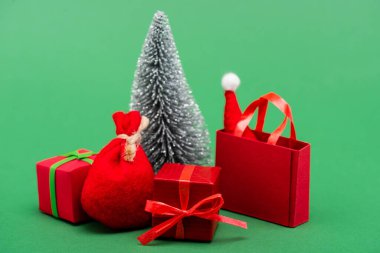 Gümüş süslemeli Noel ağacı hediye kutularının yanında, çuval ve alışveriş çantası ve yeşil şapkalı Noel Baba