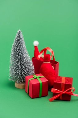 Süslü gümüş Noel ağacı hediye kutularının yanında, çuval ve alışveriş çantası ve yeşil şapkalı Noel Baba