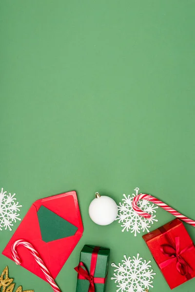 ギフトボックスのトップビュー カード付き封筒 クリスマスボール コピースペースと緑の背景にキャンディーの杖と装飾的な雪の結晶 — ストック写真