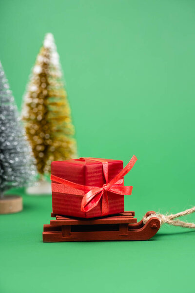selective focus of silver and golden decorative christmas trees near sled with gift box on green
