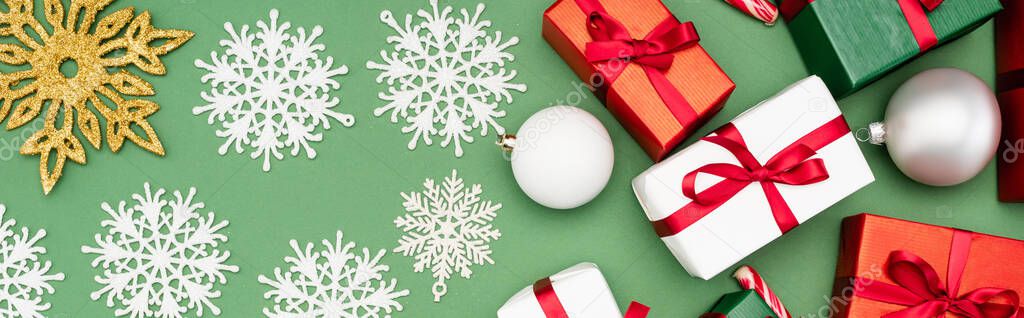 panoramic shot of colorful gift boxes, christmas balls and decorative snowflakes on green background, top view