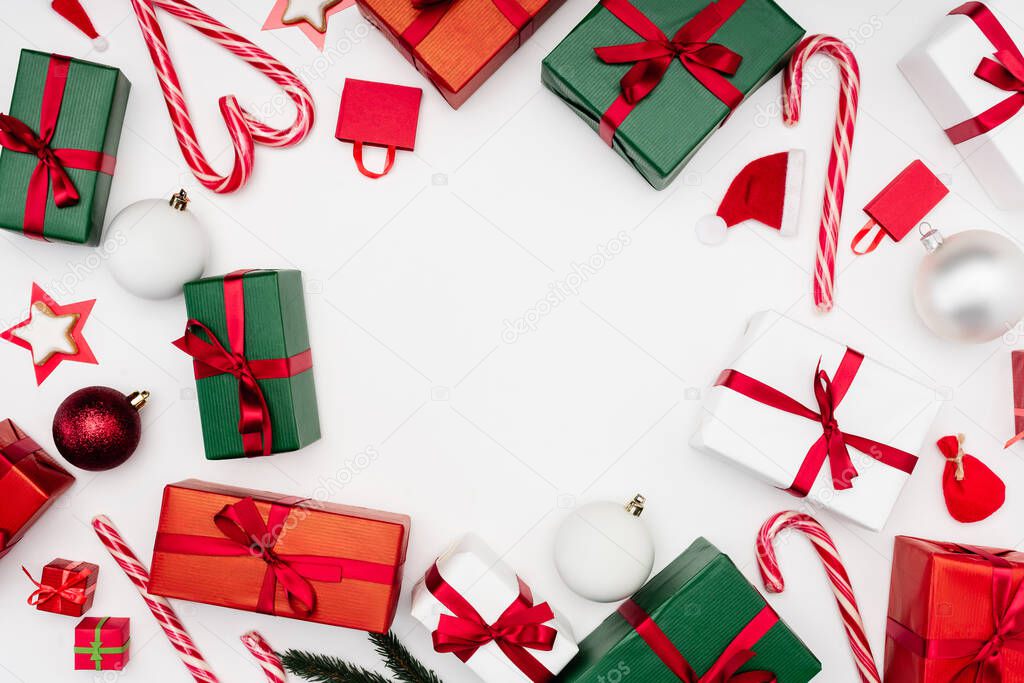 frame of multicolored gift boxes, candy canes and christmas baubles on white