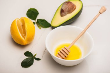 Taze avokado, limon, ballı kase ve beyaz gül yapraklarının yanında ahşap damlatıcı.
