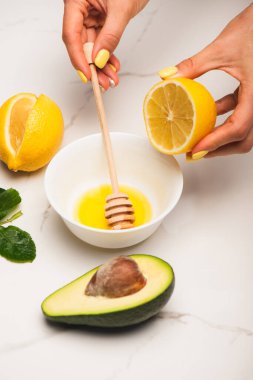 Kesik avokado ve gül yapraklarının yanında balla limonu karıştıran bir kadın manzarası.