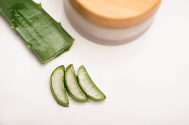 Aloe vera yaprağı, kesilmiş parçaların yanında ve beyaz üzerine ev yapımı kozmetik krem konteynır.