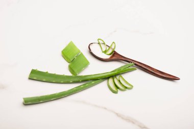 aloe vera dilimlerin yanında yapraklar ve beyaz üzerine ev yapımı kozmetik krem sürülmüş tahta kaşık.