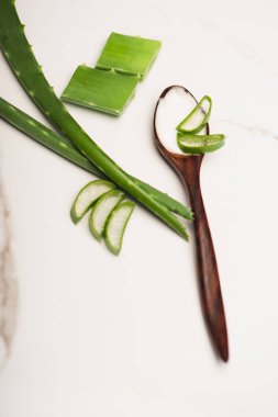 Dilimlenmiş aloe vera yapraklarının yanında ev yapımı kozmetik kremle ahşap kaşık manzarası.