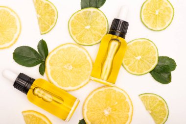 top view of bottles with citrus essential oil near lemon and lime slices near rose leaves on white clipart