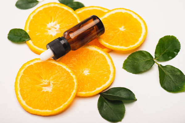 bottle of citrus essence on juicy orange slices near rose leaves on white