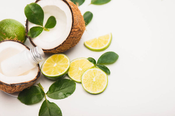 sliced lime, rose leaves, coconut halves and milk on white background