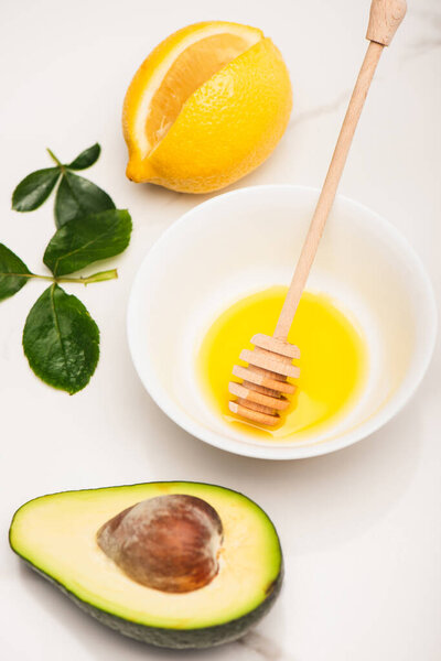 свежий сочный авокадо, лимон, миска с медом и деревянной ложкой рядом с листьями роз на белом