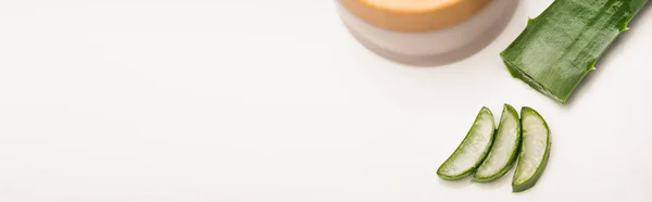 白いバナーに手作りの化粧品クリームを水和物で容器の近くにカットアロエベラの葉のスライス — ストック写真