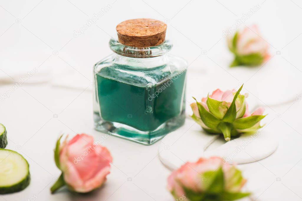 corked bottle of homemade tonic near tea roses and cotton pads on white blurred background