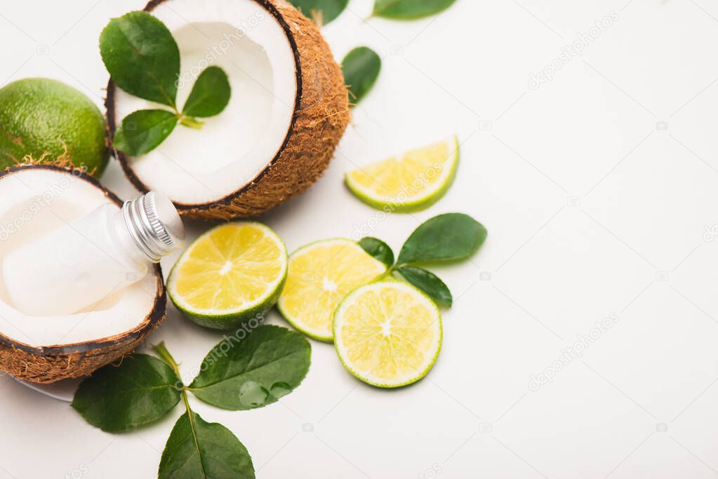 sliced lime, rose leaves, coconut halves and milk on white background