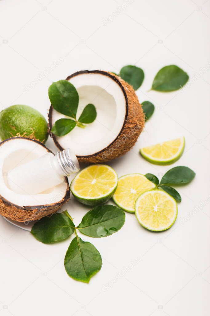 coconut halves with bottle of milk near lime and rose leaves on white background