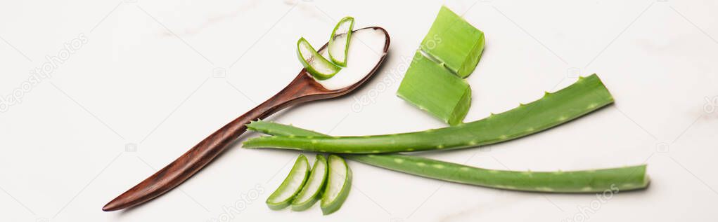 aloe vera leaves, pieces and slices near wooden spoon with homemade cosmetic cream on white, banner