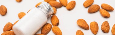 bottle with homemade lotion surrounded by almonds on white, banner clipart