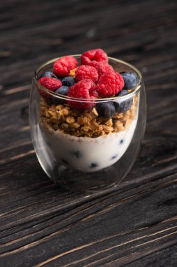 delicious granola with berries and yogurt in glass cup on wooden surface clipart