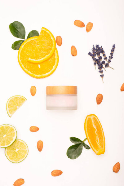 top view of homemade cosmetic cream near sliced orange and lime, almonds, lavender twigs and rose leaves on white