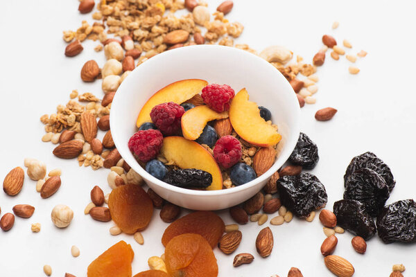 delicious granola with nuts, berries and fruits in bowl on white