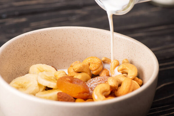йогурт льется на вкусную мюсли с орехами, бананом и сушеными абрикосами в миске