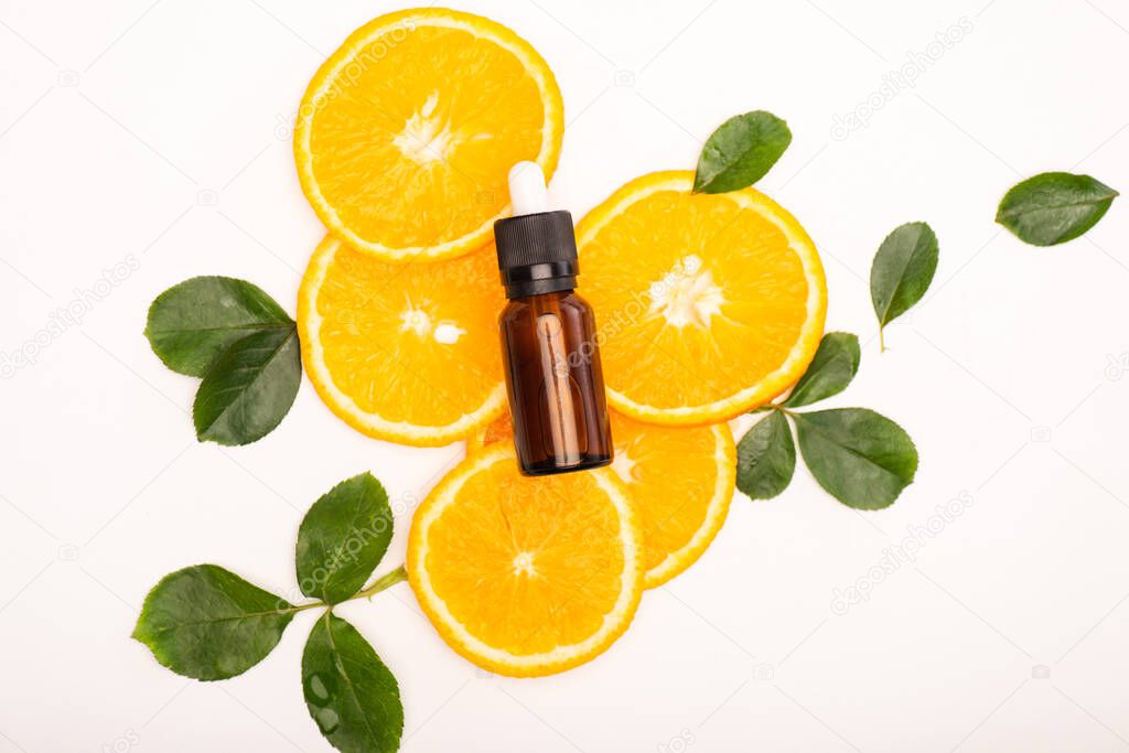 top view of bottle with citrus essential oil and juicy orange slices near rose leaves on white