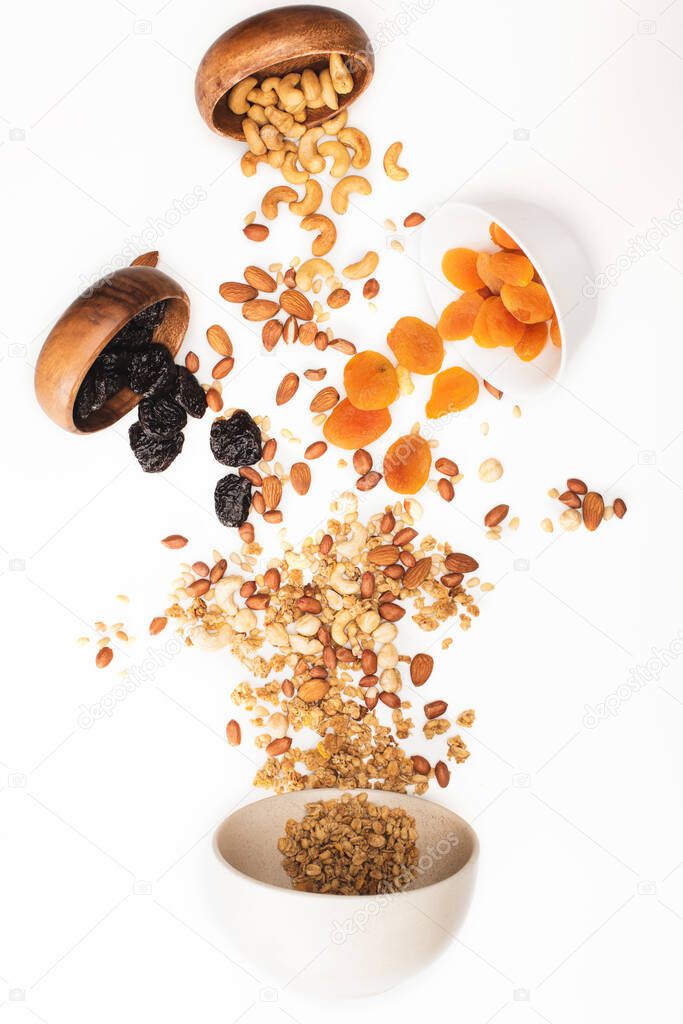 top view of delicious granola with nuts and dried fruits scattered from bowls isolated on white