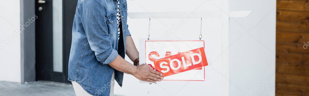 Cropped view of man holding sign with sold lettering near house, banner