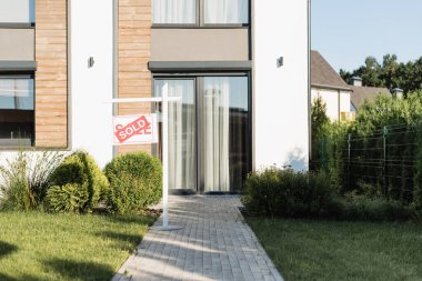 Front facade of modern house near lawn and sign with sold lettering clipart