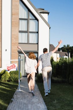 Back view of couple with hands in air near sign with sold lettering and modern house clipart