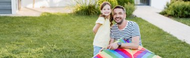 Happy daughter and father with kite looking at camera on lawn, banner clipart