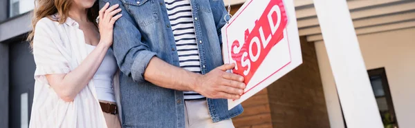 Cropped view of couple near sign with sold lettering, banner