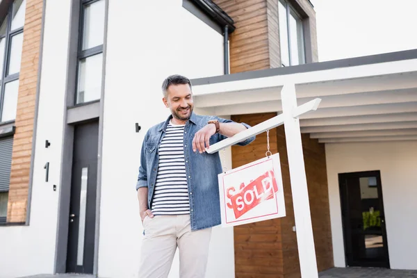 笑顔男で手でポケットに見てサインとともに販売レタリング近く家 — ストック写真