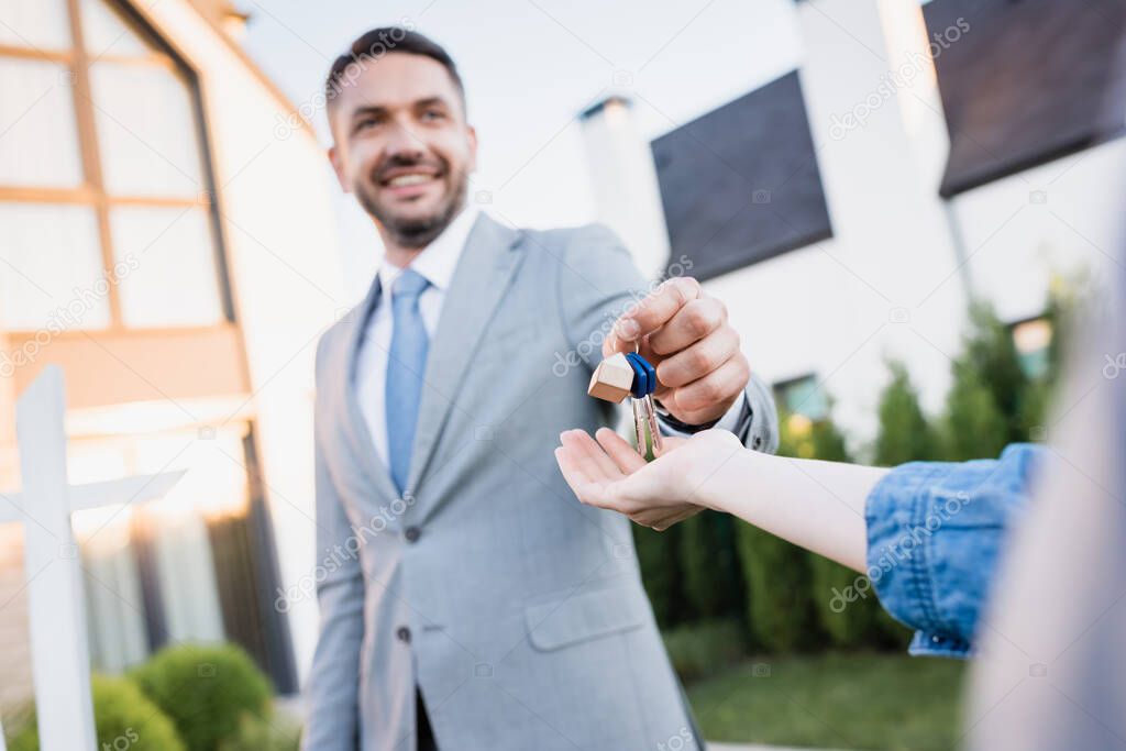 Smiling real estate agent giving keys to woman with blurred houses on background